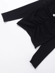 Detail of black knit top with side ruched texture and sparkling rhinestone button accent