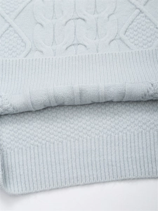 Detail eines hellblauen Zopfstrickpullovers mit Strukturmuster und Rippstrickbündchen