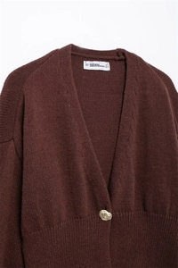 Dettaglio del cardigan in maglia marrone con scollo a V e bottone dorato unico