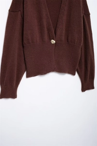 Dettaglio del cardigan in maglia marrone scuro con bottone dorato e polsini a costine