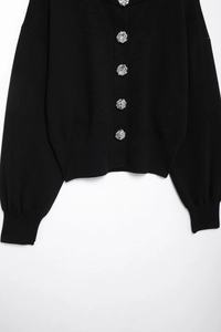 Close-up of black knitted cardigan featuring textured silver metal buttons and ribbed cuffs