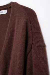 Dettaglio di un cardigan in maglia marrone scuro con scollo a V, trama del tessuto ed etichetta