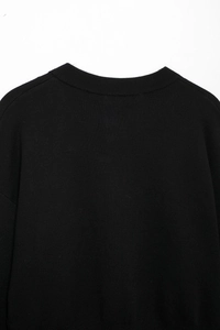 Close-up detail of the black knitted sweater showing ribbed neckline and fine fabric texture