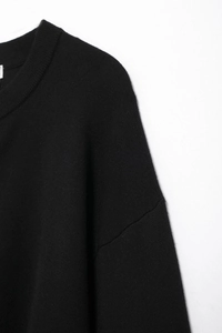 Detail of the crew neckline and fine knit texture on a black long sleeve sweater