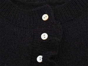 Dettaglio del cardigan nero in maglia con bottoni in madreperla e scollatura rotonda a costine