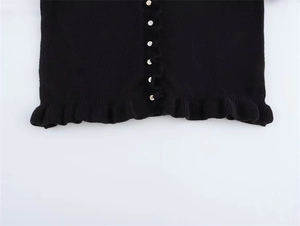 Dettaglio del cardigan in maglia nera con bottoni in conchiglia e orlo con volant