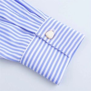Détail du poignet d'une chemise à rayures bleues et blanches avec bouton triangle doré