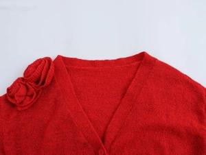 Detailansicht des V-Ausschnitts und der 3D-Blumenakzente dieser roten Strickjacke