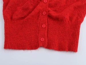 Nahaufnahme der roten Strickjacke mit geripptem Saum und passenden Knöpfen auf Textur