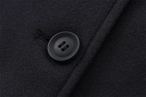 Close-up of black felt wool jacket fabric with matte four-hole button and stitching details