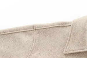 Detail shot of the shoulder seam and wool blend texture of the beige felt coat