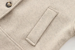 Detail of oatmeal wool coat featuring wood texture button and neat welt pocket