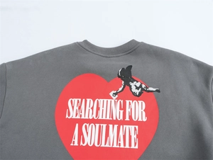 Dettaglio della stampa Cupido e del testo 'Searching For A Soulmate' sulla felpa grigia