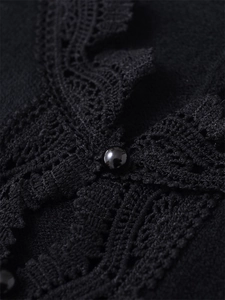 Close-up of elegant black lace trim and polished pearl button on the knit cardigan sleeve