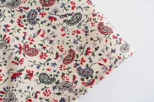 Dettaglio della stampa floreale paisley su abito crema a maniche lunghe con orlo arrotolato