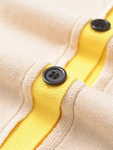 Détail macro du cardigan tricoté bicolore beige et jaune avec boutons noirs ronds