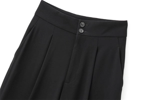 Détail du pantalon noir taille haute avec fermeture à double bouton et plis à la taille