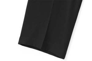 Gros plan d'un pantalon noir montrant des plis verticaux nets et une texture de tissu de qualité