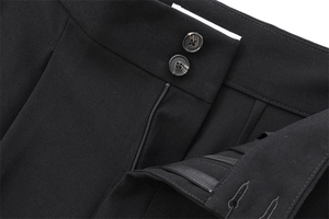 Vue macro d'un pantalon noir avec doubles boutons en écaille et détails de braguette zippée