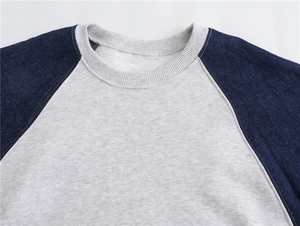 Detail of raglan sleeves and ribbed crew neck on gray and denim patchwork sweatshirt