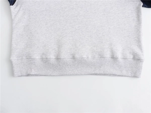 Detail of ribbed hem and color-block stitching on gray denim patchwork sweatshirt