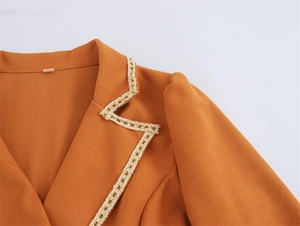 Detailed close-up of orange blazer lapel with white lace trim and twill fabric texture