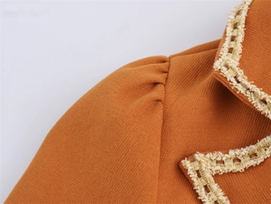Close-up of knit dress collar with golden thread lace trim and puffed shoulder detail