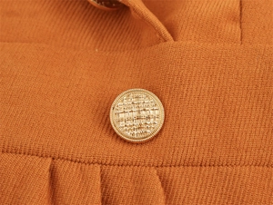 Macro detail of golden textured button on burnt orange twill fabric dress