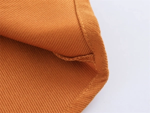 Macro shot of ginger yellow pleated fabric with fine stitching on the garment hem