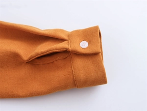 Detail of ginger corduroy dress sleeve with white button and textured fabric finish