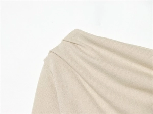 Close-up of beige textured fabric featuring elegant pleated shoulder details on the blouse