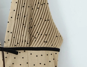 Detail of pleated beige dress with black flocking polka dots and velvet ribbon accent