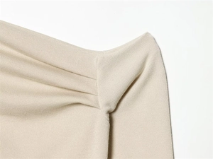 Macro detail of the beige knitted fabric showing elegant pleats and fine texture