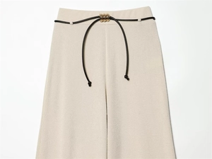 Detail of high-waisted off-white trousers with fine texture and gold beaded metal buckle