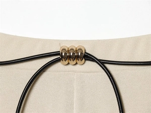 Macro view of beige knit fabric waist detail with black cord and gold triple-ring buckle