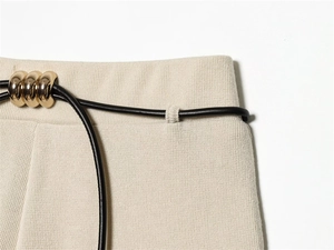 Detail of cream ribbed knit fabric and black leather waist cord with gold metal rings