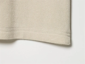 Detailed close-up of double-stitched hem and waffle knit texture on off-white knit top