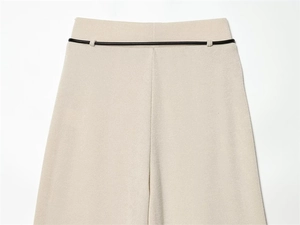 Detail of oat-colored knitted trousers featuring a slim black minimalist leather belt