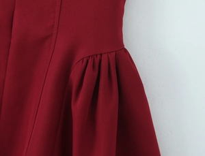 Détail de la robe rouge foncé montrant les coutures et les fronces à la taille