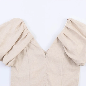 Close-up of beige linen dress featuring deep V-neckline with zipper and puff sleeves