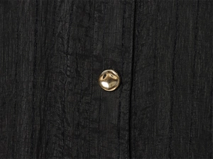 Close-up of black pleated fabric texture featuring a decorative golden irregular metal button