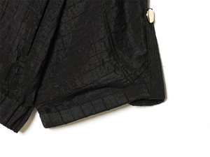 Detail of pleated black shirt fabric with a polished gold button and fine stitching