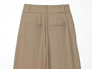 Detail of high-waist taupe trousers with back welt pockets and vertical creases