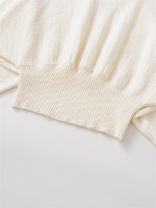Close-up of cream knit sweater showing detailed ribbed cuff and textured fabric