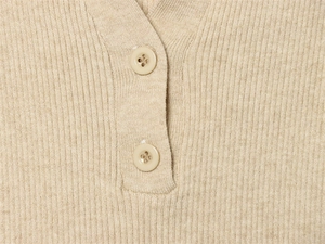 Dettaglio ravvicinato della trama in maglia a coste e bottoni di una polo beige