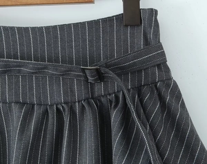Detail of dark grey pinstripe trousers featuring a high waist and adjustable metal buckle belt