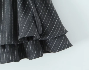 Detailed close-up of dark grey pinstripe fabric with layered ruffle design and fine texture