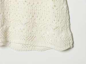 Close-up of white knitted dress featuring intricate hollow crochet and scalloped hem