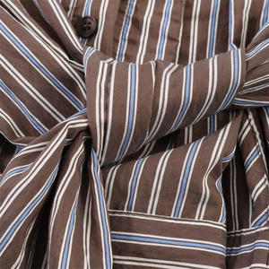 Detail van gestreepte bruine stof met knoopsluiting en strikceintuur in de taille