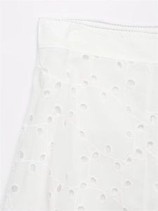 Close-up detail of white eyelet embroidery on a summer skirt featuring floral textures